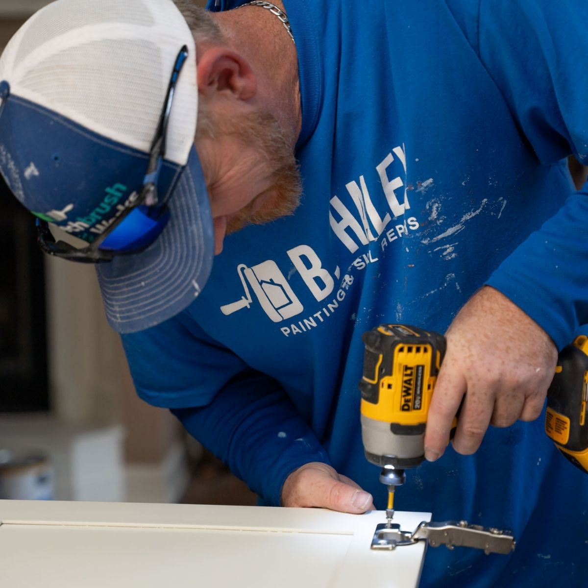 A man using a drill to drill a white painted cabinet.