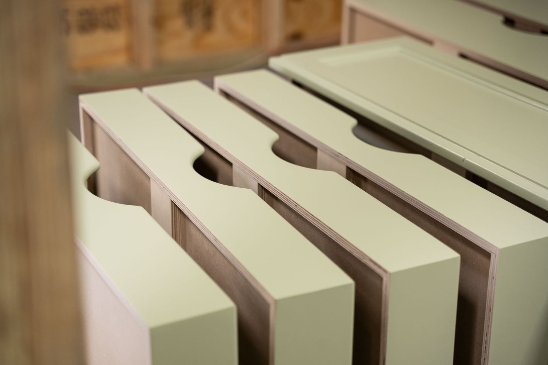 Several white cabinet drawers with curved handles are stacked vertically in a workshop, with unfinished walls in the background.