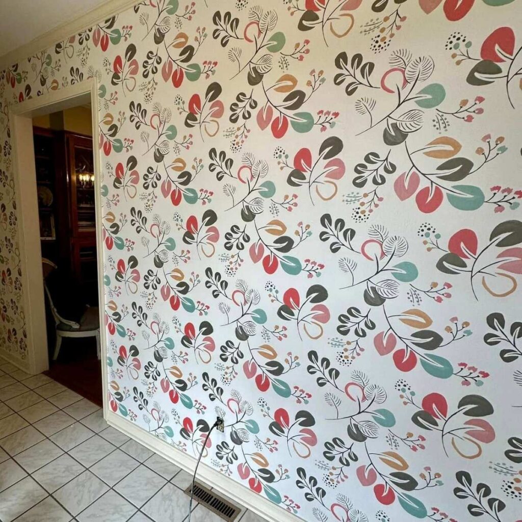A wall covered with colorful, vintage-style floral wallpaper in shades of red, green, orange, and black, next to a tiled floor and an open doorway leading to another room. A cord is visible near the baseboard.