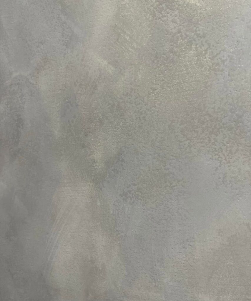 A close-up of a textured gray wall with subtle variations in shade and a slightly rough, uneven surface pattern.