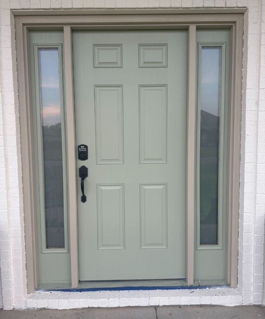 A light green front door with a keypad lock and black handle, flanked by two tall, narrow glass panels, set in a white brick exterior.